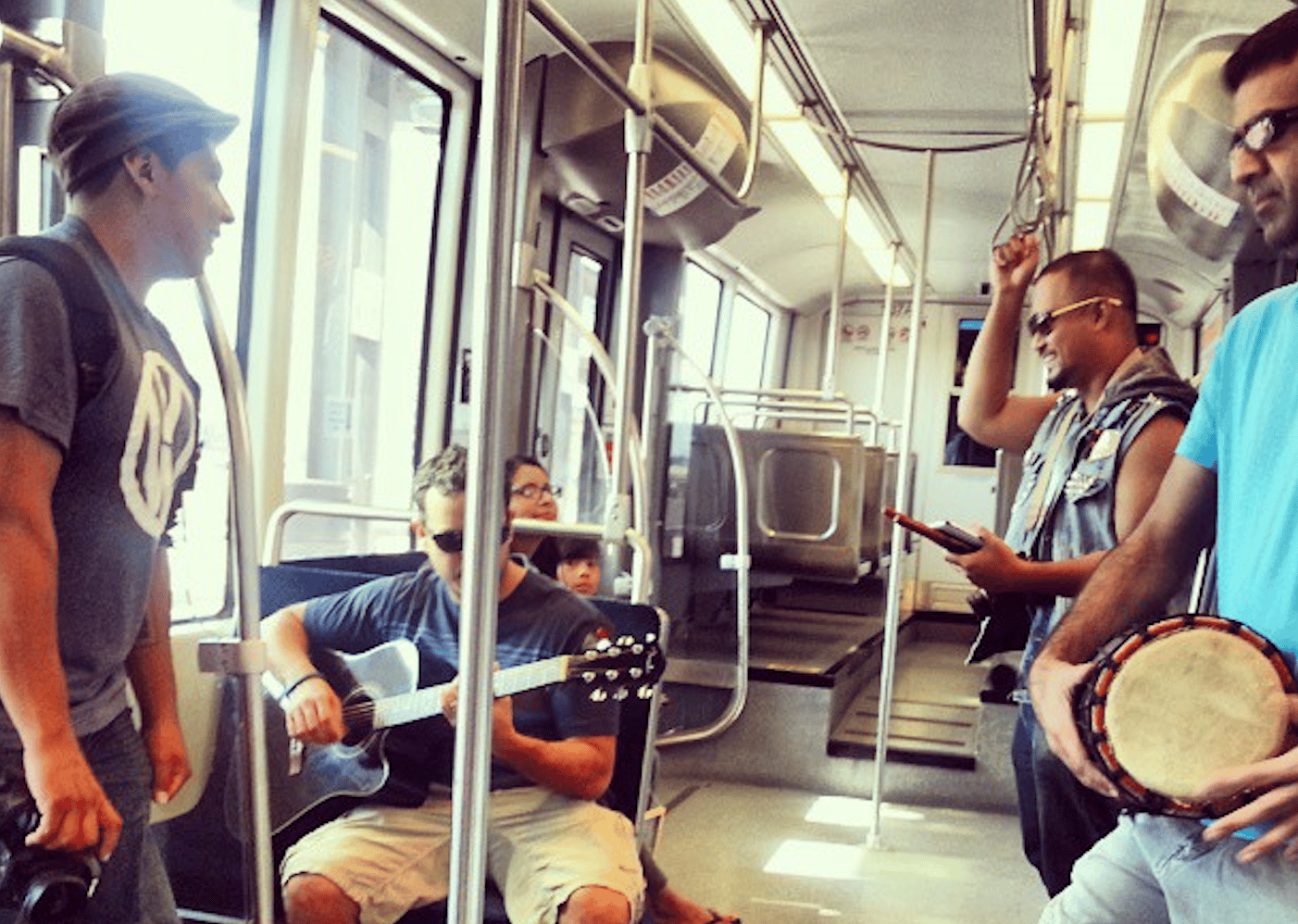 5 people holding musical instruments and a camera sitting and standing on a Houston metro rail